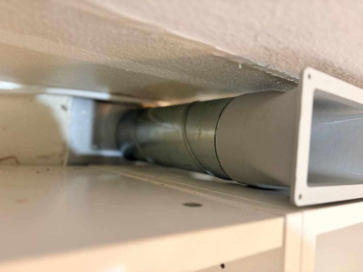 Adapter połączony z rurą spiro, ułożony w szczelinie nad szafkami